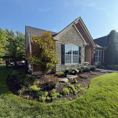Charming stone-front house with vibrant landscaping and clear blue sky.