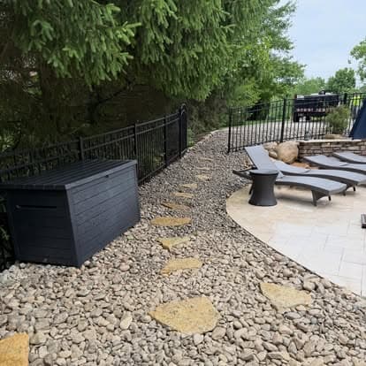 Scenic pathway with stone steps, gravel, black storage box, and lounge chairs in backyard.