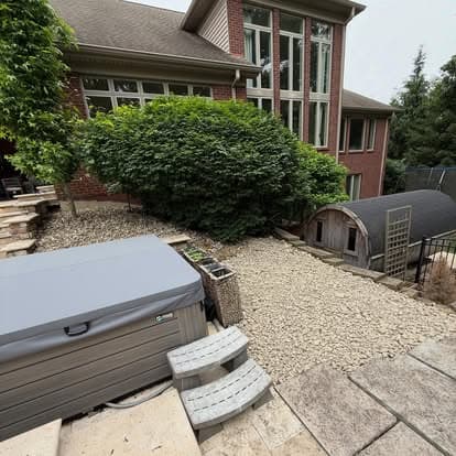 Backyard view featuring a hot tub, landscaped stone pathway, and a green hedge near a home.