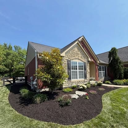 Charming suburban home with stone facade, lush landscaping, and vibrant flower beds.
