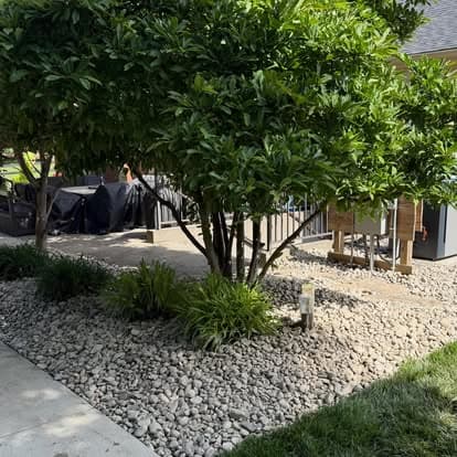 Lush landscaped garden with a tree, gravel path, and outdoor seating area.