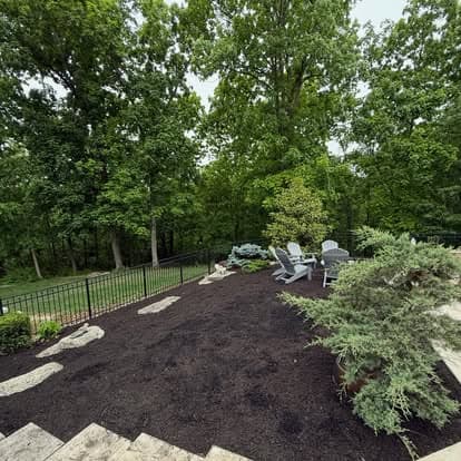 Lush backyard landscaping with seating area, trees, and decorative stones.