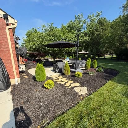 Elegant backyard patio with seating, umbrellas, and neatly trimmed hedges under a clear blue sky.