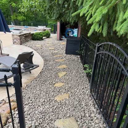 Garden pathway with stone stepping stones and gravel, bordered by a black iron fence.