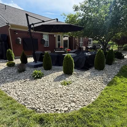 Outdoor patio with umbrella, decorative rocks, and lush green landscaping.